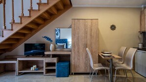 Ein modernes Wohnzimmer mit einer Holztreppe, einem Fernseher, einem Essbereich mit Stühlen und einem Schrank.