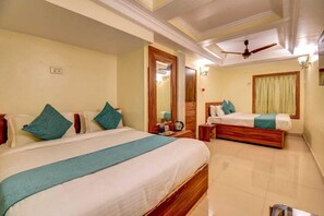 A hotel room with two beds, a ceiling fan, a mirror, and a window with curtains. - Ishwar Inn Resort (Mahabaleshwar)