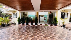 A covered outdoor area with a tiled floor, potted plants, and a building entrance.
