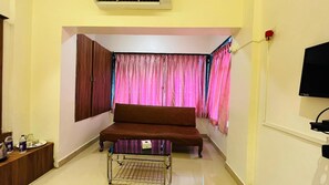 A room with a brown sofa, a small table, a TV, and curtains.