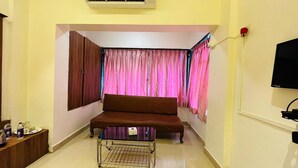 A room with a brown sofa, a small table, a TV, and curtains.