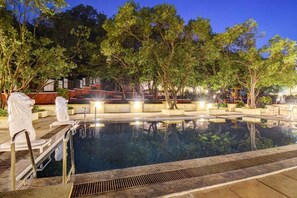 A swimming pool with steps leading into it, surrounded by trees and outdoor seating areas.