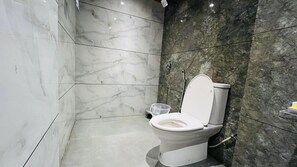 A bathroom with a toilet, marble walls, and a shower area.