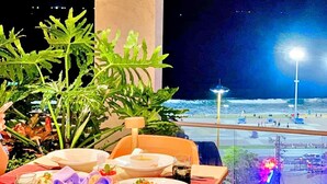 A table set for dining with a view of the beach and cityscape at night. - Hanz Business Suite Oceanus Condotel (Bac Nha Trang)