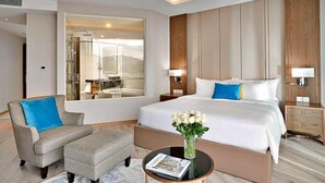 A hotel room with a bed, a chair, a nightstand, a bedside table with a magazine, and a large mirror reflecting a bathroom. - Hanz Business Suite Oceanus Condotel (Bac Nha Trang)