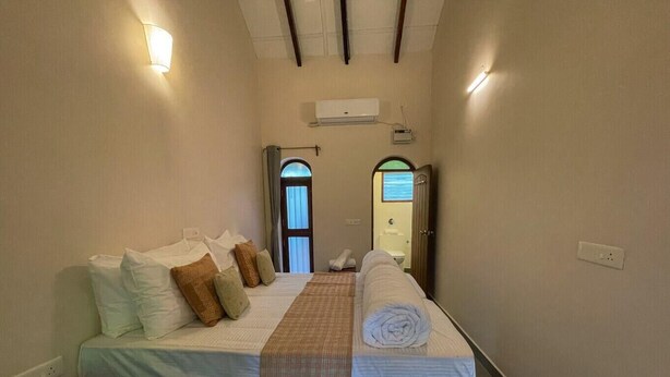 Habitación de hotel con cama, almohadas, un banco, una toalla, una ventana y un equipo de aire acondicionado.
