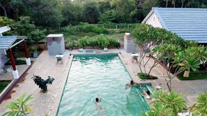 Una piscina rectangular con una solana empavedada alrededor, bancos y plantas en macetas.