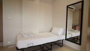 A single bed with white bedding in a room with a large mirror and a wooden wardrobe. - Shrigo Hotel Rudra Palace (Udaipur)