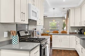 A modern kitchen with white cabinets, a gas stove, and a microwave.