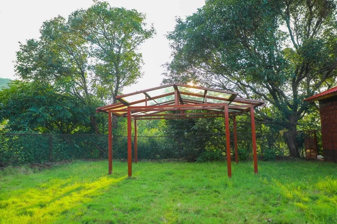 Ein Gazebo mit transparenter Dachkonstruktion, umgeben von üppigem Grün und Bäumen.