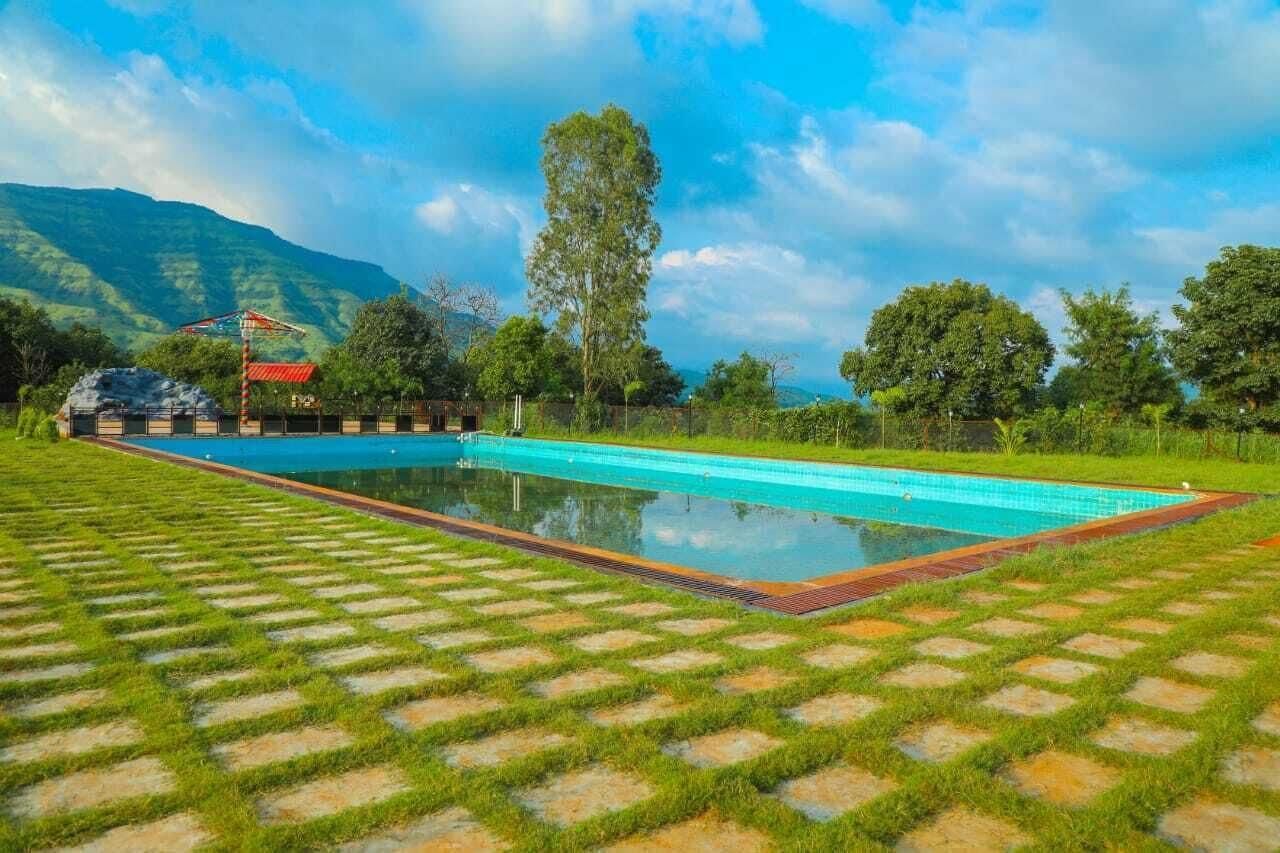 A swimming pool with a paved deck, surrounded by greenery and mountains in the background.