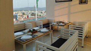 Un espace repas avec des tables et des chaises, une vue sur le paysage urbain et un drapeau à l’extérieur.