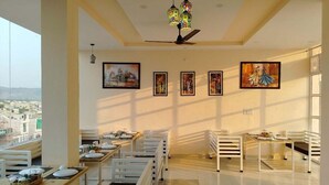 A dining area with tables and chairs, artwork on the walls, and a view of the city. - Skyza Rooftop Lodge (Jaipur)