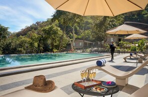 A poolside area with a table set for a meal, a drink tray, and a hat. - Kumbhalgarh Valley Resort Kumbhalgarh (Kumbhalgarh)