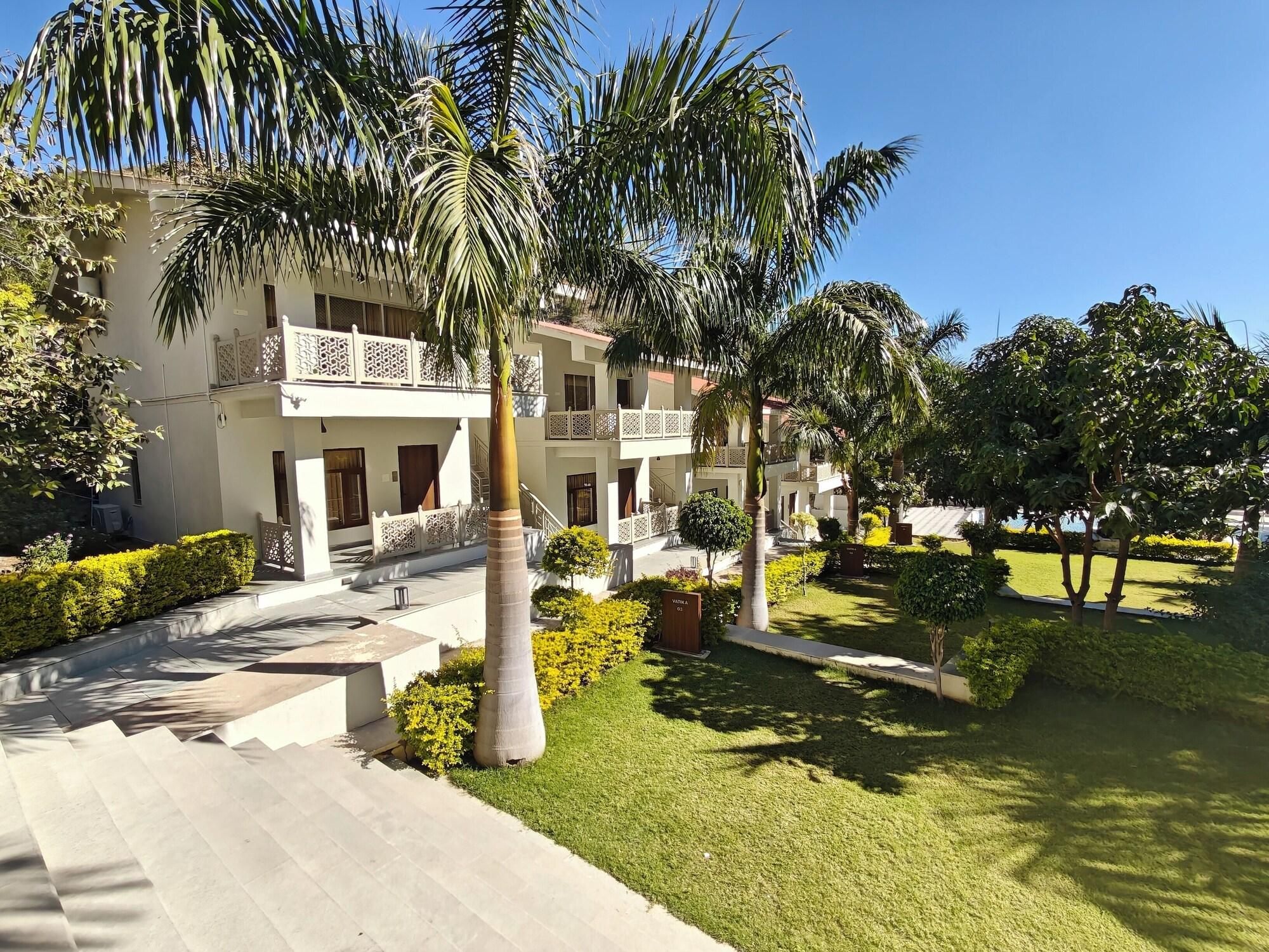 Un hotel de varios pisos con un patio central, palmeras y un césped bien cuidado.