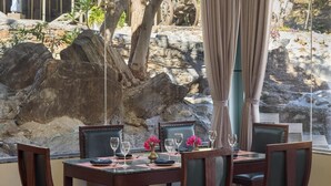 A dining area with a table set for four, surrounded by chairs, with a view of a rocky landscape and trees. - Kumbhalgarh Valley Resort Kumbhalgarh (Kumbhalgarh)