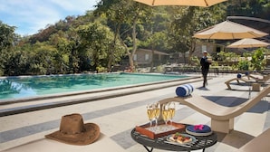 A poolside area with a table set for a meal, a drink tray, and a hat. - Kumbhalgarh Valley Resort Kumbhalgarh (Kumbhalgarh)