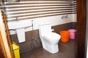 A bathroom with a toilet, sink, and shower. There are two buckets, one orange and one pink. - Ac Mist (Kanayannur)