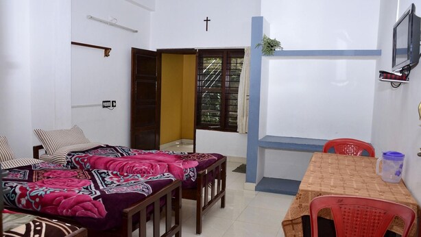 A room with a bed, a desk, a chair, a window with a view, and a cross on the wall.