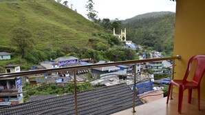 A balcony with a view of a hillside, a red plastic chair, and a metal railing.
