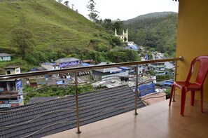 A balcony with a view of a hillside, a red plastic chair, and a metal railing.
