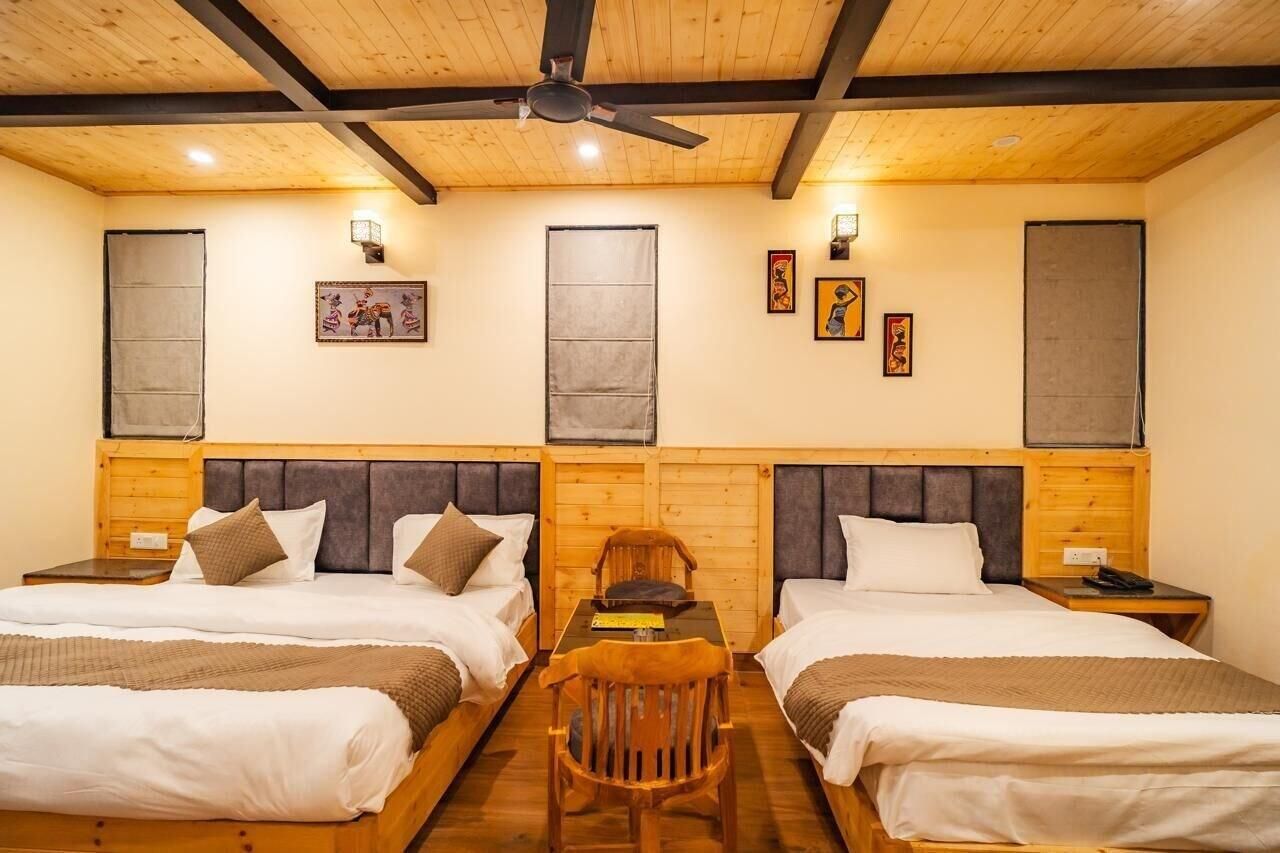 A room with two beds, a table, a chair, a ceiling fan, and artwork on the walls.
