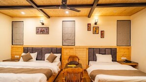 A room with two beds, a table, a chair, a ceiling fan, and artwork on the walls. - Hotel Winterfell Mussoorie (Dehradun)