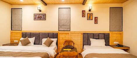 A room with two beds, a table, a chair, a ceiling fan, and artwork on the walls.