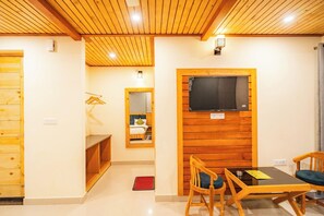 Ein Zimmer mit Holzboden, einem Bett mit Kopfteil, einem an einer Holzwand befestigten Fernseher, einem Tisch mit Stühlen und einem Holzschrank.