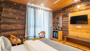 A log cabin room with a bed, two chairs, a small table, a TV, and a kitchenette. - Hotel Winterfell Mussoorie (Dehradun)