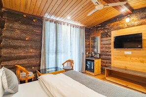 A log cabin room with a bed, two chairs, a small table, a TV, and a kitchenette. - Hotel Winterfell Mussoorie (Dehradun)