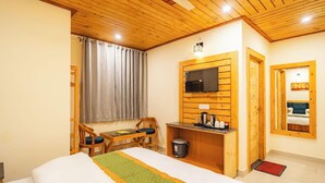 Een hotelkamer met een bed, een bureau met een televisie, een stoel en een raam met gordijnen.