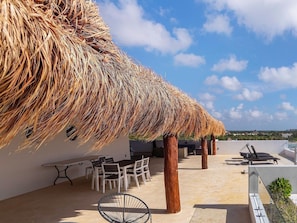 Una terraza en la azotea con techo de paja, mobiliario exterior y vistas al paisaje.