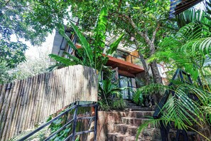 Una escalera que lleva a un edificio con valla de bambú y abundante vegetación.