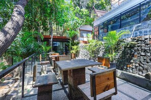 An outdoor seating area with stone tables and wooden chairs, surrounded by lush greenery and a stone wall. - Fabhotel Prime Amazonika Boutique Resort (Arpora)
