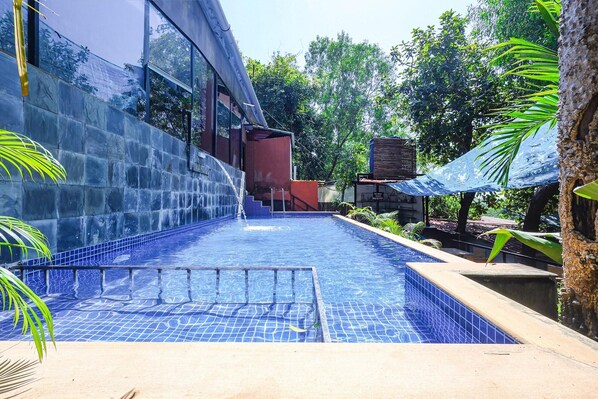Una piscina con borde de azulejos, rodeada de vegetación y un edificio con grandes ventanales.
