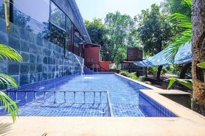 A swimming pool with a tiled edge, surrounded by greenery and a building with large windows. - Fabhotel Prime Amazonika Boutique Resort (Arpora)