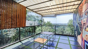 A balcony with a view of greenery, a table, and a mural. - Fabhotel Prime Amazonika Boutique Resort (Arpora)