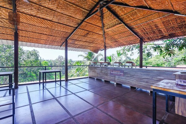 A covered outdoor area with a bar and restaurant, tiled flooring, and a view of palm trees. - Fabhotel Prime Amazonika Boutique Resort (Arpora)