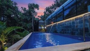 A swimming pool with a waterfall feature, surrounded by lush greenery and a modern building with large windows. - Fabhotel Prime Amazonika Boutique Resort (Arpora)