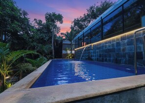 A swimming pool with a waterfall feature, surrounded by lush greenery and a modern building with large windows. - Fabhotel Prime Amazonika Boutique Resort (Arpora)