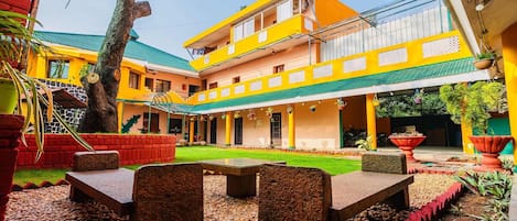 A courtyard with a building featuring a green roof, a covered seating area with tables, and a well-maintained lawn.