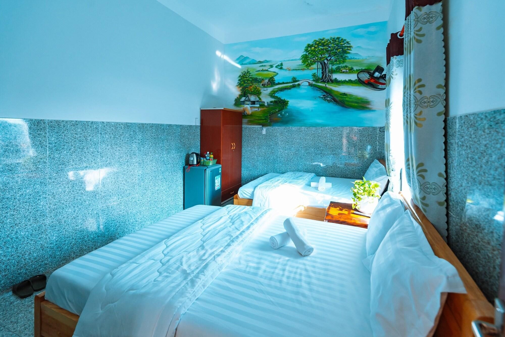 A hotel room with a bed, a small table, a wall-mounted fan, and a painting of a landscape.