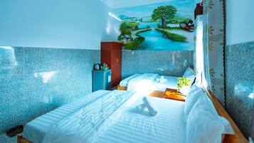 A hotel room with a bed, a small table, a wall-mounted fan, and a painting of a landscape.