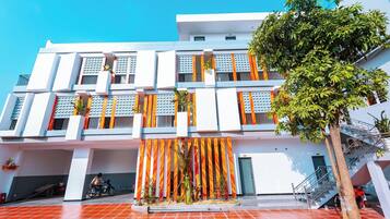 A multi-story building with a modern architectural design, featuring balconies, a staircase, and a tiled ground floor.