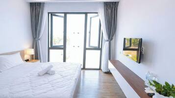 A hotel room with a bed, a TV mounted on the wall, a bedside table with a lamp, and a view through a glass door.
