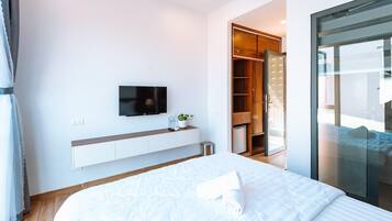 A modern bedroom with a bed, a TV, a wardrobe, and a sliding glass door to a balcony.