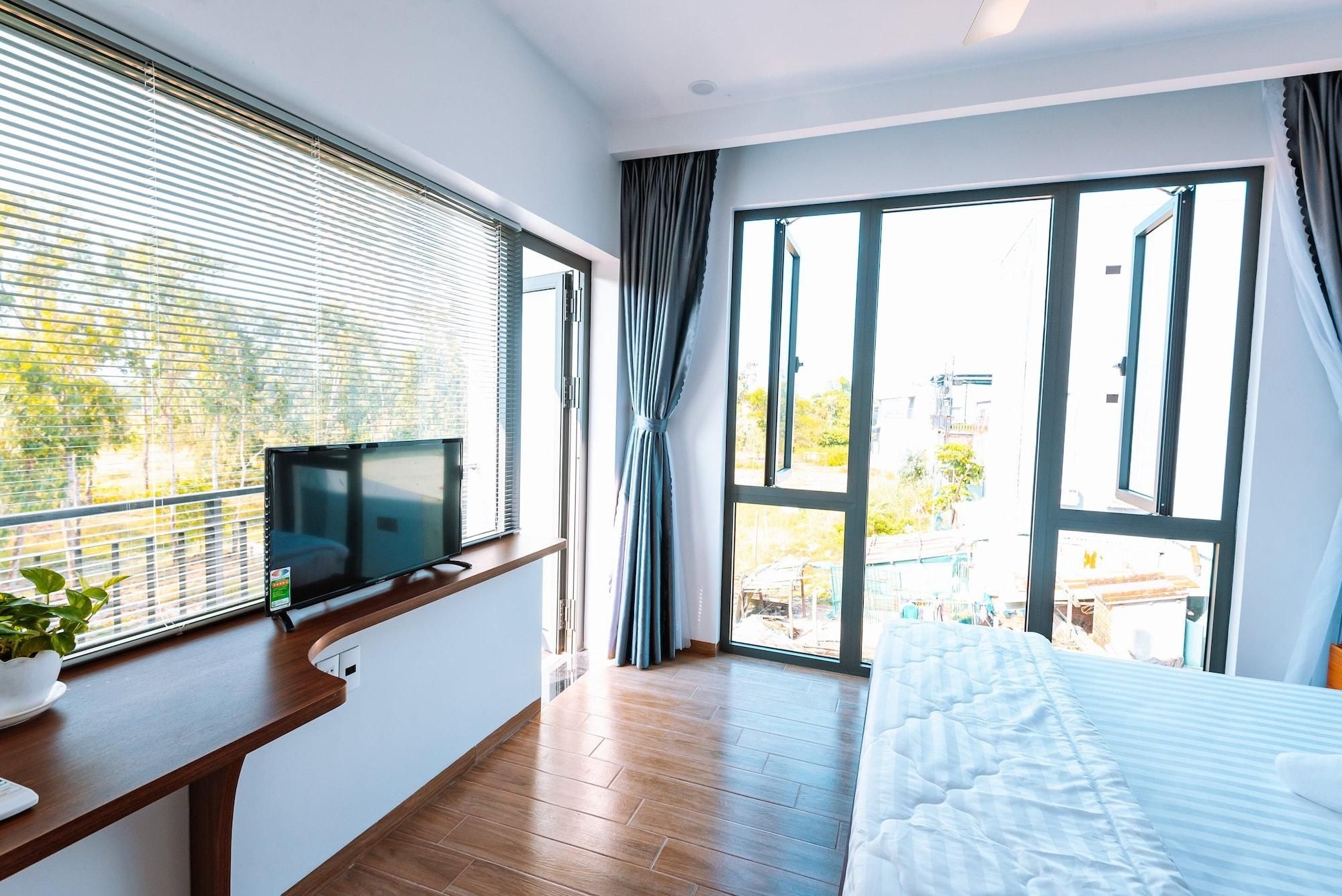 A modern bedroom with a large window, a TV on a wooden console, a bed, and a potted plant.