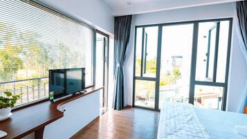 A modern bedroom with a large window, a TV on a wooden console, a bed, and a potted plant.