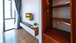 A modern room with a wooden floor, a mounted TV, a small plant, and a window with curtains. - Ngochoa Hotel (Da Nang Municipality)